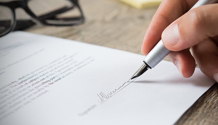 Hand signing a document with pen.