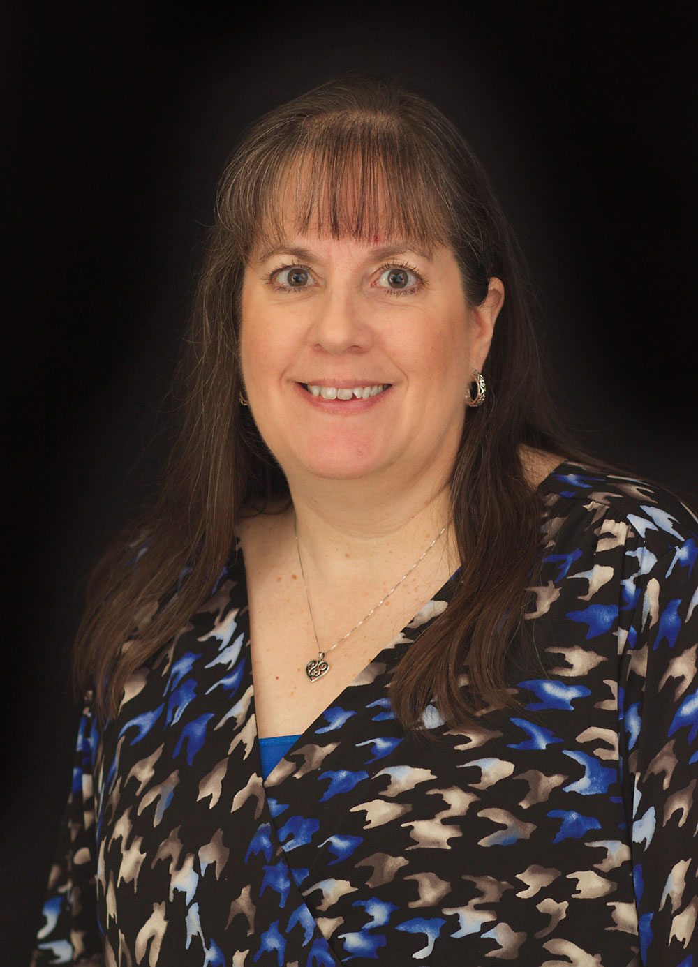 Woman in patterned blouse, neutral background.